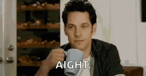 A Man Is Sitting At A Table Drinking A Cup Of Coffee And Saying Aight . GIF