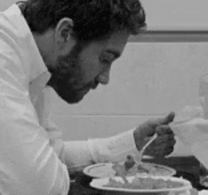 A Man Is Sitting At A Table Eating A Plate Of Food With A Fork . GIF
