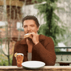 A Man Is Sitting At A Table Eating A Sandwich And Drinking A Glass Of Iced Tea GIF
