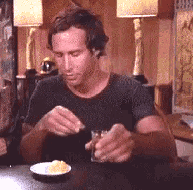 A Man Is Sitting At A Table Eating A Sandwich And Drinking A Glass Of Whiskey . GIF