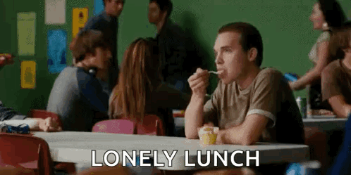 A Man Is Sitting At A Table Eating A Spoonful Of Food In A Cafeteria . GIF