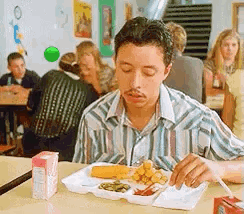 a man is sitting at a table eating a tray of food in a cafeteria .