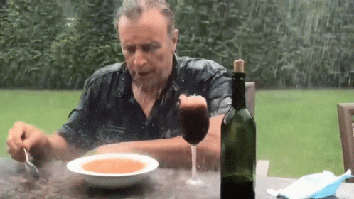 A Man Is Sitting At A Table Eating Soup And Drinking Wine GIF