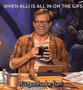 A Man Is Sitting At A Table Holding A Cup Of Coffee And A Tablet Computer . GIF