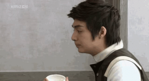 A Man Is Sitting At A Table Holding A Cup Of Coffee In His Hand . GIF