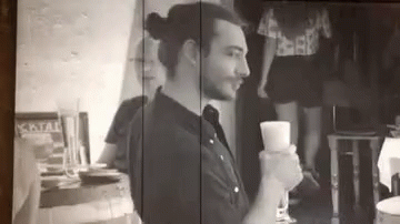 A Man Is Sitting At A Table Holding A Glass Of Wine In A Black And White Photo . GIF