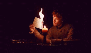 A Man Is Sitting At A Table Holding A Piece Of Paper That Is Burning GIF