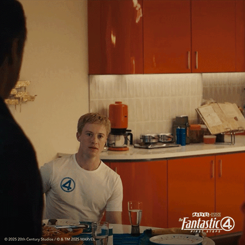 A Man Is Sitting At A Table In A Kitchen Wearing A Fantastic 4 Shirt GIF