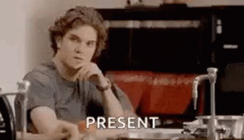 A Man Is Sitting At A Table In A Kitchen With His Hand On His Chin And The Word Present . GIF
