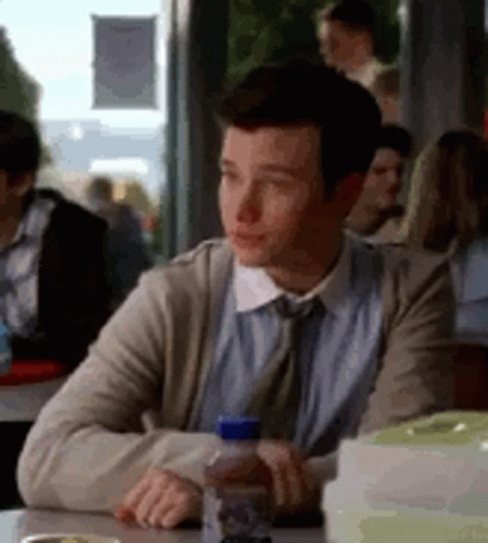 A Man Is Sitting At A Table In A Restaurant With A Bottle Of Water In His Hand . GIF