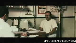 A Man Is Sitting At A Table Talking To Another Man . GIF