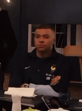 A Man Is Sitting At A Table Wearing A Black Nike Jacket With A Rooster On It GIF