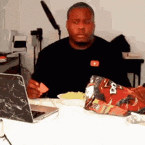 A Man Is Sitting At A Table With A Bag Of Doritos On It GIF