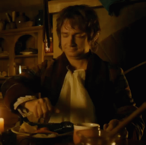 A Man Is Sitting At A Table With A Bowl Of Food And A Spoon GIF