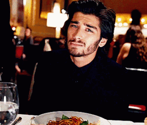 A Man Is Sitting At A Table With A Bowl Of Spaghetti On It GIF