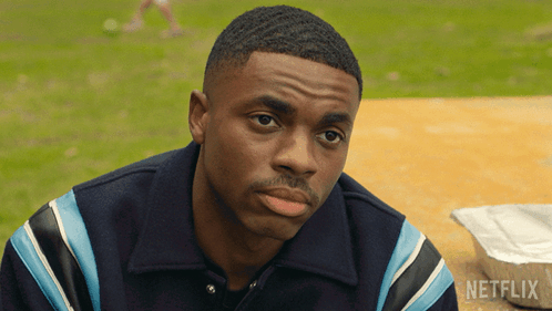 A Man Is Sitting At A Table With A Box Of Netflix Behind Him GIF