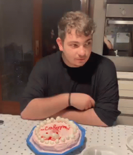 A Man Is Sitting At A Table With A Cake On It And Looking At It . GIF