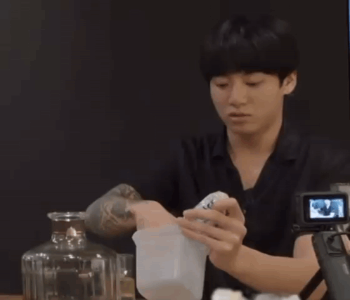 A Man Is Sitting At A Table With A Camera And A Bottle Of Alcohol GIF