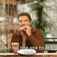 A Man Is Sitting At A Table With A Glass Of Beer And A Plate Of Food And Waiting For Her To Text Him . GIF