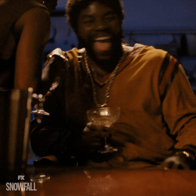A Man Is Sitting At A Table With A Glass Of Wine In His Hand And The Words Fx Snowfall On The Bottom Right GIF