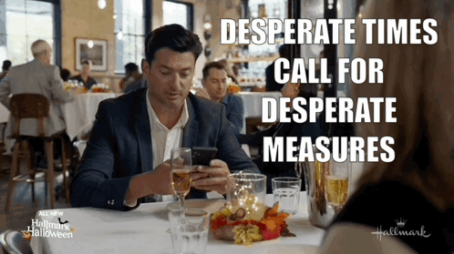 A Man Is Sitting At A Table With A Glass Of Wine Looking At His Phone With The Words Desperate Times Call For Desperate GIF