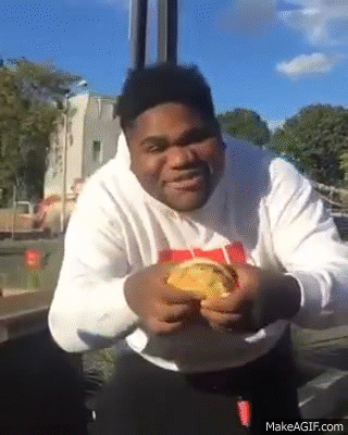 A Man Is Sitting At A Table With A Hamburger In His Hand . GIF