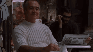 A Man Is Sitting At A Table With A Newspaper That Says Commentatore On It GIF