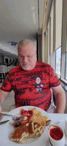 A Man Is Sitting At A Table With A Plate Of Food And A T-Shirt That Says " No " GIF