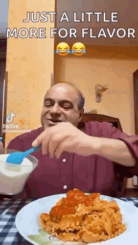 A Man Is Sitting At A Table With A Plate Of Pasta And A Spoon . GIF