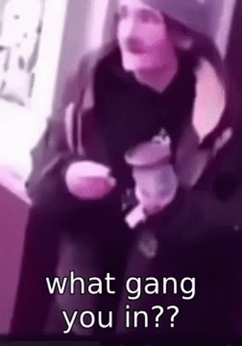 A Man Is Sitting Down Holding A Cup Of Coffee And Asking What Gang You Are In . GIF