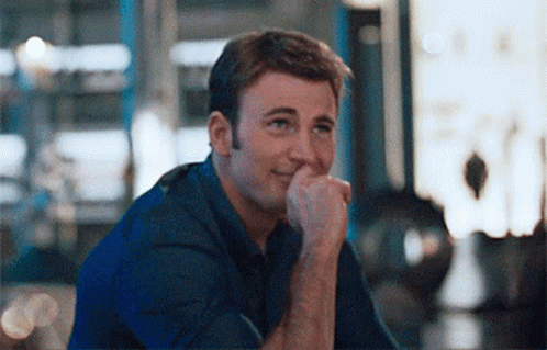 A Man Is Sitting Down With His Hand On His Chin And Smiling . GIF