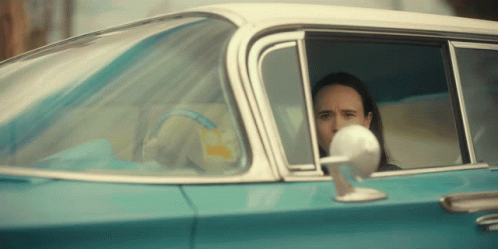 A Man Is Sitting In A Blue Car And Looking Out The Window At The Camera GIF