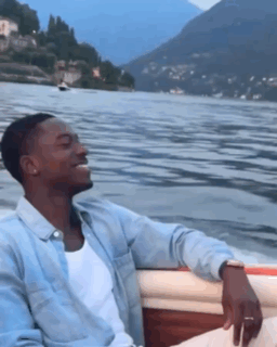 A Man Is Sitting In A Boat On A Lake GIF