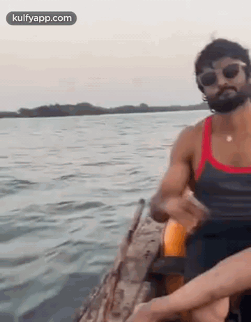 A Man Is Sitting In A Boat On A Lake . GIF