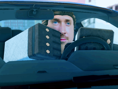 A Man Is Sitting In A Car With A Box Behind Him GIF