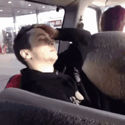 A Man Is Sitting In A Car With His Eyes Closed And His Hand On His Forehead GIF