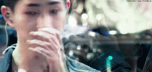 A Man Is Sitting In A Car With His Hands On His Face And Looking Out The Window . GIF