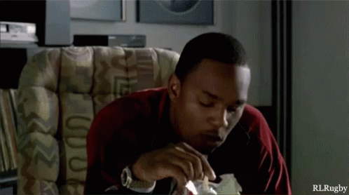 A Man Is Sitting In A Chair Eating A Piece Of Bread With Rlrugby Written On The Bottom GIF