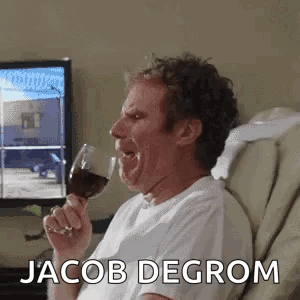A Man Is Sitting In A Chair Holding A Glass Of Wine And Making A Funny Face . GIF