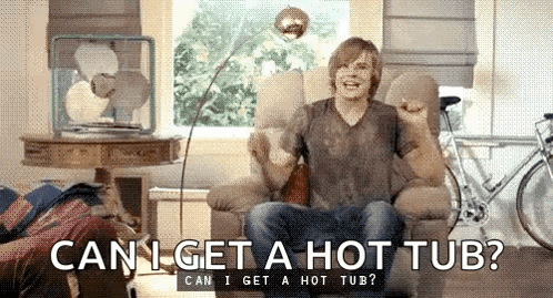 A Man Is Sitting In A Chair In A Living Room Asking Can I Get A Hot Tub . GIF