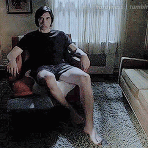 A Man Is Sitting In A Chair In A Living Room Without A Shirt On . GIF