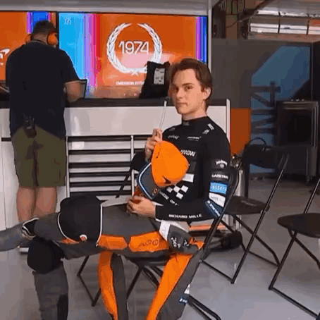 A Man Is Sitting In A Chair In Front Of A 1974 Sign GIF