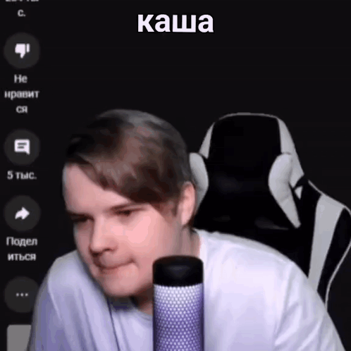 A Man Is Sitting In A Chair In Front Of A Microphone With A Foreign Language On The Screen . GIF