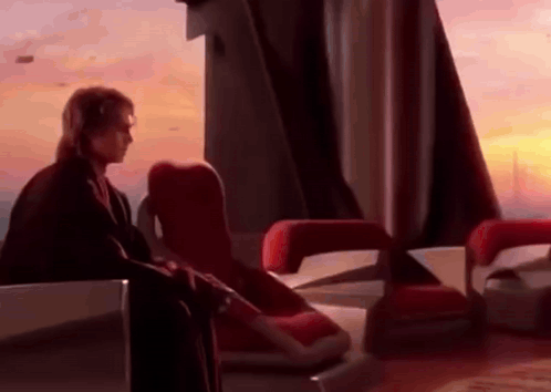 A Man Is Sitting In A Chair In Front Of A Window In A Room . GIF