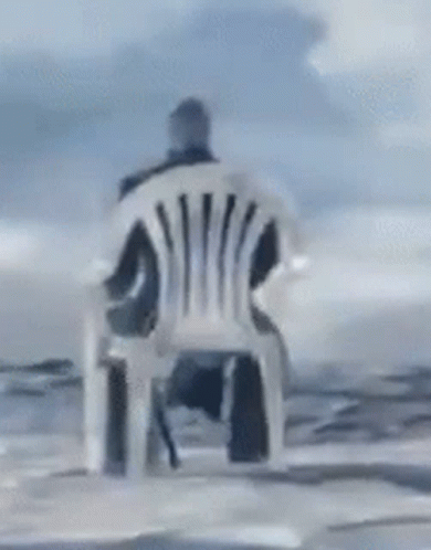 A Man Is Sitting In A Chair In Front Of The Ocean GIF