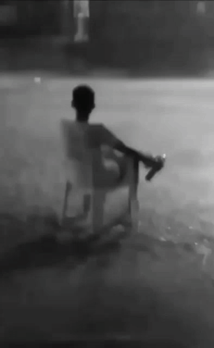 A Man Is Sitting In A Chair In The Rain Holding A Bottle . GIF