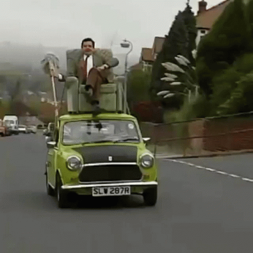 A Man Is Sitting In A Chair On Top Of A Green Car . GIF