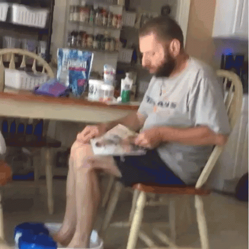 A Man Is Sitting In A Chair Reading A Book GIF