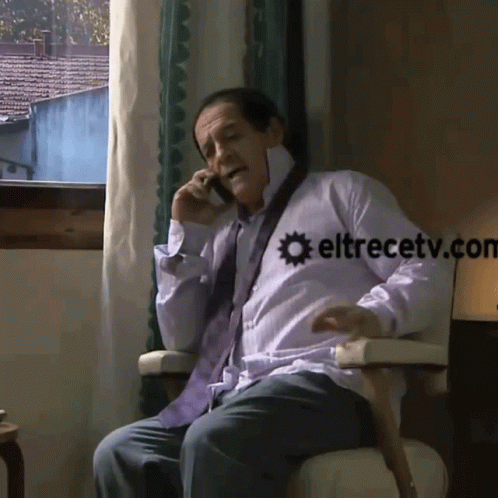 A Man Is Sitting In A Chair Talking On A Cell Phone With Eltrecetv.com Written On The Bottom GIF