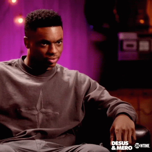 A Man Is Sitting In A Chair Wearing A Sweatshirt That Says " Desus & Mero " GIF